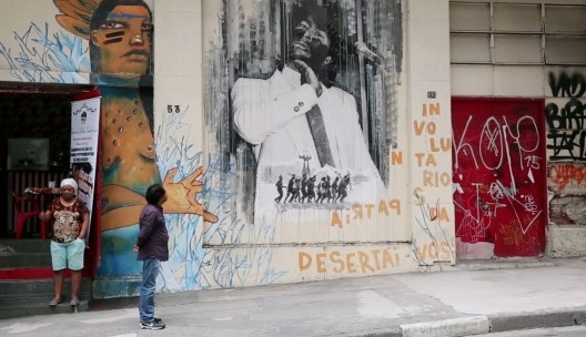 Ailton Krenak observando grafite que reproduz sua manifestação na Assembleia Constituinte em 1987, fotograma do filme “Ailton Krenak, o sonho da pedra”