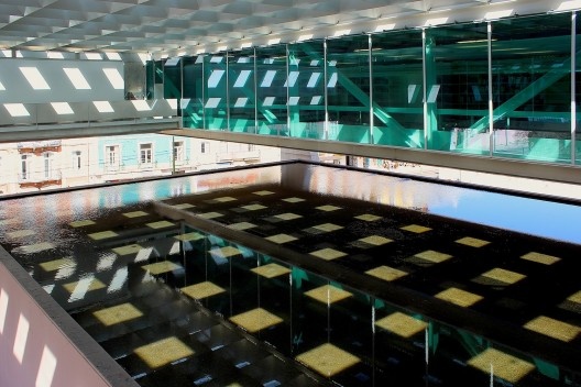 A luz da cobertura em grelha refletida no espelho d`água sobre o auditório