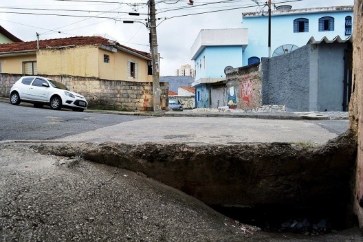 Córrego oculto, entre antigas pontes, o ruído rouco das águas oclusas invade a rua por meio de bocas de lobo