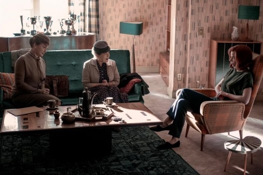 Sala de estar, estampa nos papéis de parede, no tapete e no estofado da poltrona. Cena do filme O Gambito da Rainha, direção de Scott Frank