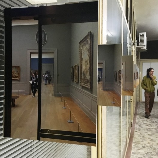 Dobra o corredor e se depara com a sequência de fotografias de Tuca Vieira, dispostas em ângulo reto na esquadria das lojas, com as pessoas fotografadas se duplicando na vidraçaria e se misturando virtualmente com os visitantes reais.