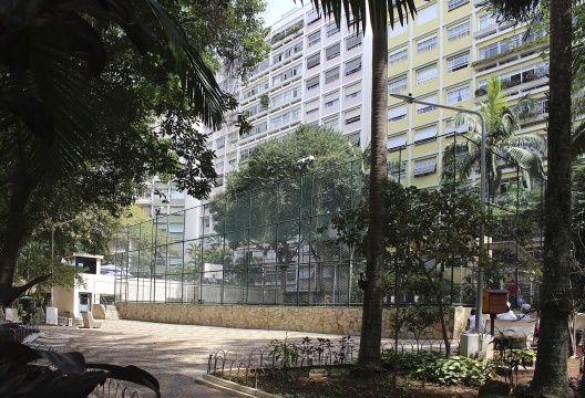 Visão parcial do paisagismo do CPA, com a quadra poliesportiva ao centro e piscina elevada em relação a cota do terreno, ao fundo