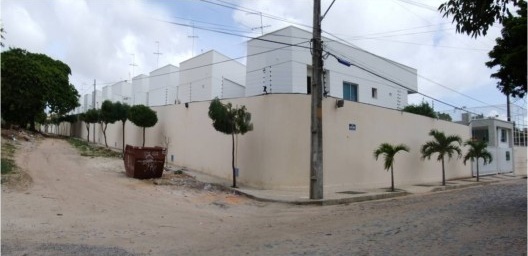 Aspecto externo do condomínio Maison Blanc em meio a vias sem pavimentação e pedra tosca