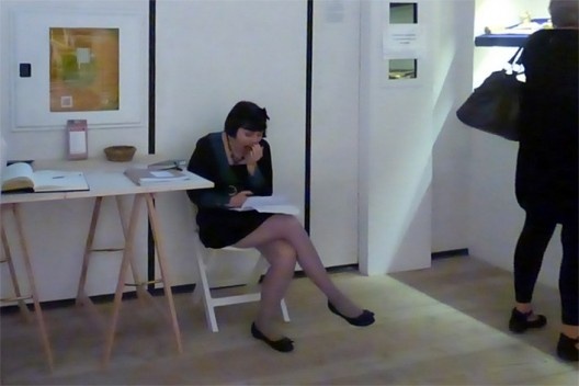 O vulto de preto passa sem ser percebido pela jovem vigia, que boceja segurando livro entediante