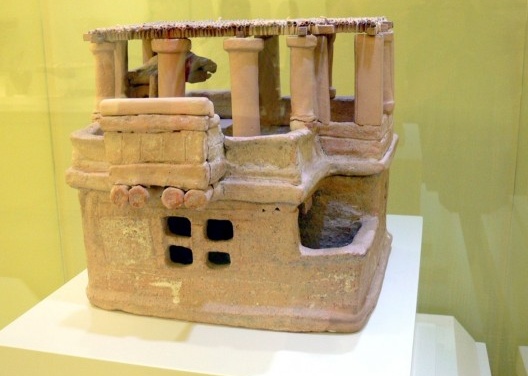 Modelo de Arkhanes; vista lateral. Datação: Minoico Médio (1.700-1.630 a.C). Material: Terracota com restos de policromia. Dimensões: Altura de cada pavimento: 15 e 18 cm; Largura: 31 cm; Profundidade: 28 cm. A cobertura do modelo foi reconstituída. Museu