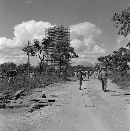 Trabalhadores no cerrado; ao fundo, o Congresso Nacional em construção, c. 1958