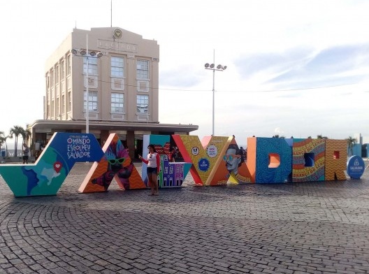Letreiro \"Salvador\" na frente do Elevador Lacerda, com a inscrição na primeira letra: “Carnaval 2019 – O mundo escolheu Salvador”. Outras letras contêm imagens de máscaras carnavalescas, fachadas coloridas das casas coloniais, retrato de Castro Alves