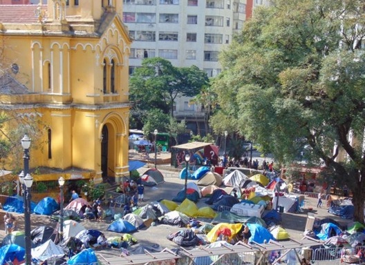 Famílias que moravam no Wilson Paes de Almeida, improvisadas em barracas, cerca de dez semanas após o desabamento do edifício, ainda desassistidas pelos agentes públicos. Localização: largo do Paissandu, ao redor da igreja Nossa Senhora do Rosário dos Hom