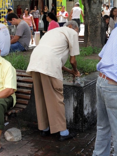 Idoso lavando as mãos em canteiro de plantas