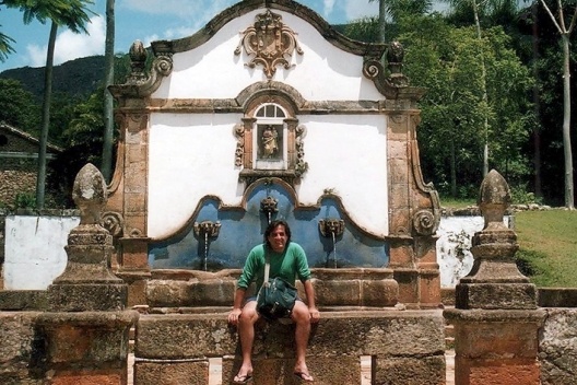 Junancy Wanderley sentado em chafariz na cidade de Tiradentes, de 1749