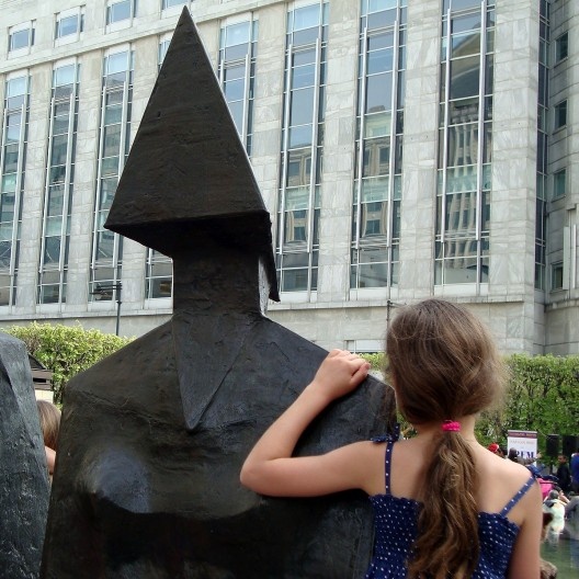 Linda em seu vestido azul, a garotinha se aconchega na figura feminina da escultura...